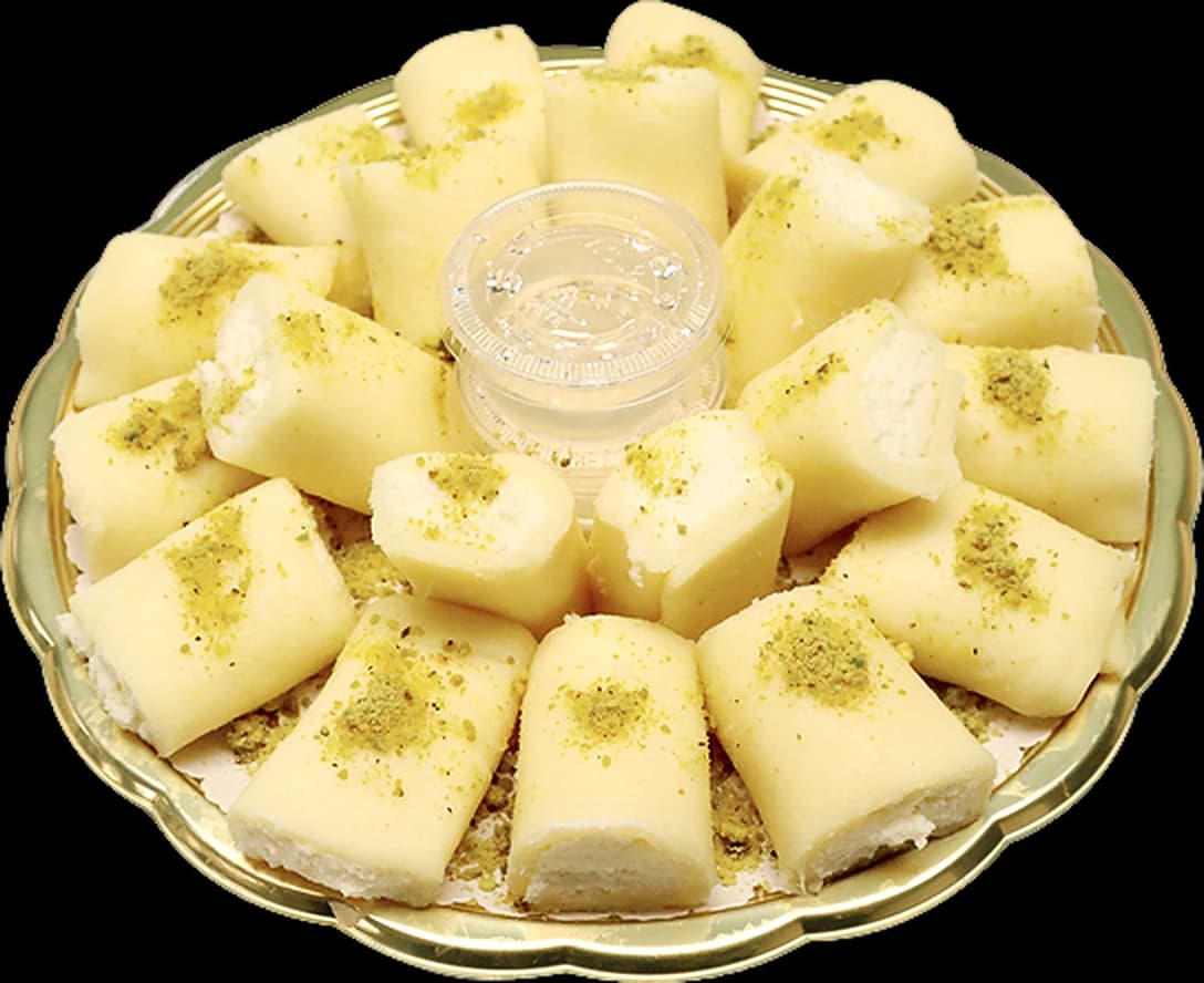 Plateau doré de halawet el jibn : rouleaux à la crème de lait poudrés de pistache, autour d’un pot de sirop